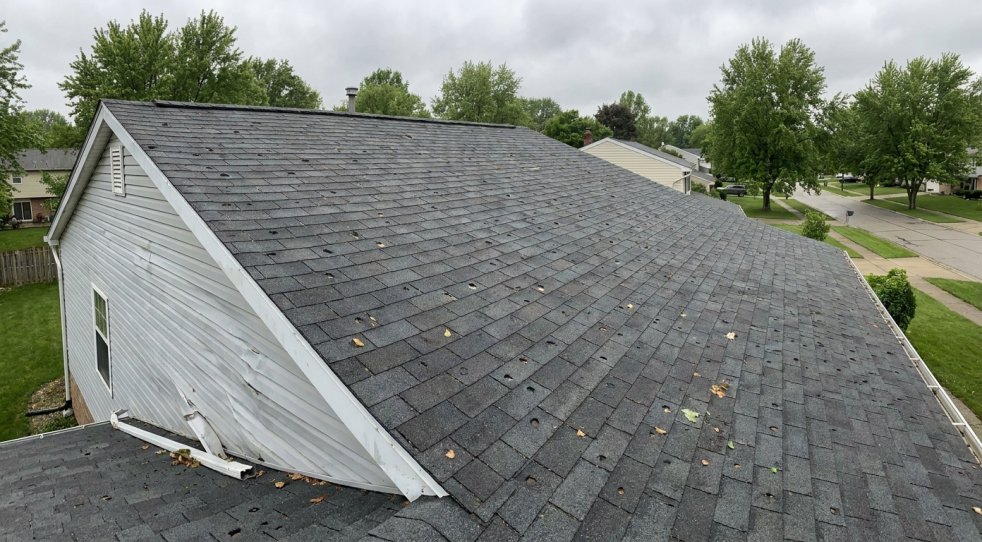 Hail-damaged asphalt shingle roof on a suburban home with scattered impact marks and loose debris